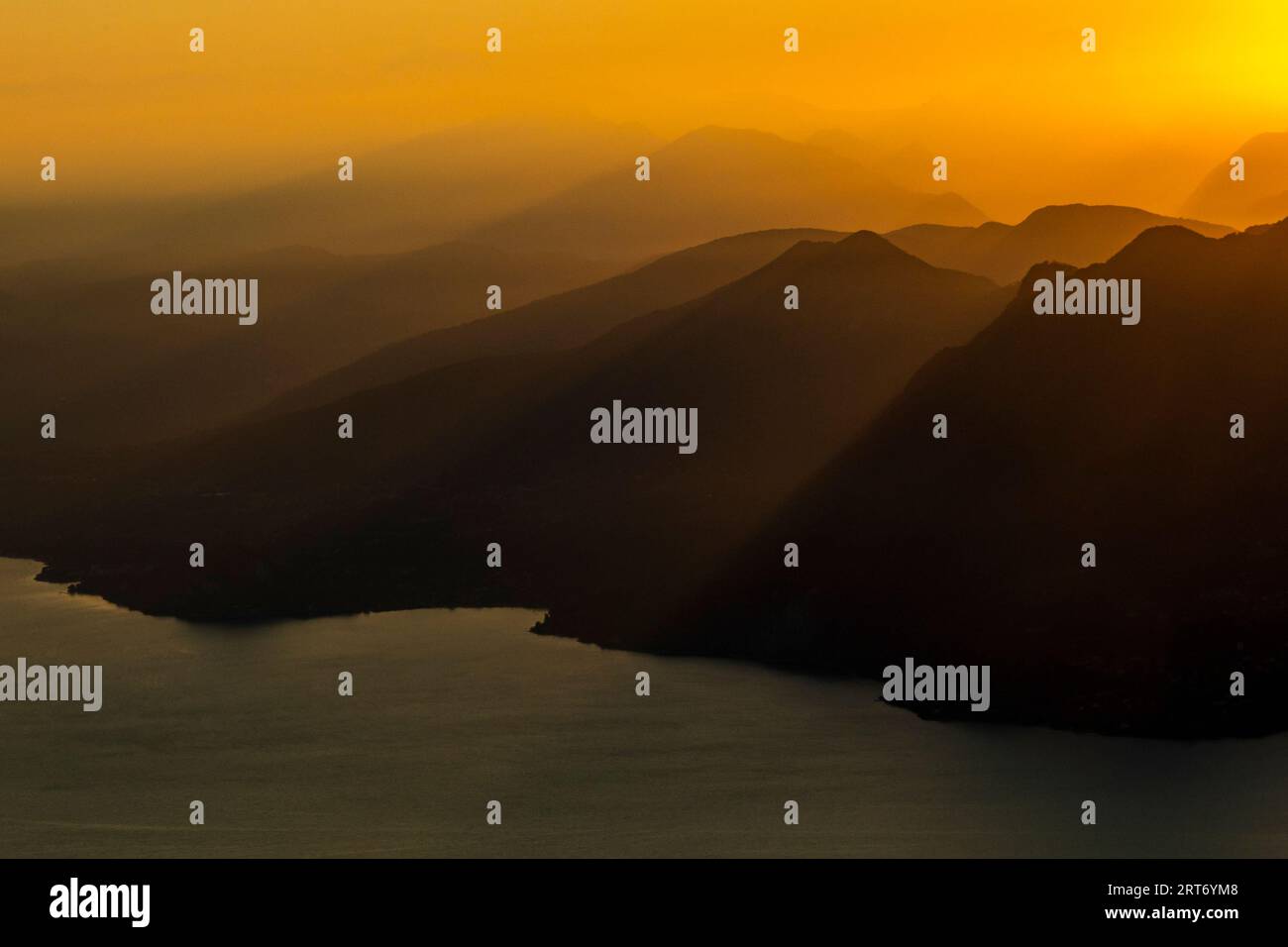 Vue pittoresque silhouette de paysage brumeux du lac et d'énormes montagnes rocheuses sous le ciel de coucher du soleil avec des nuages orange dans la frontière du lac majeur entre les deux Banque D'Images