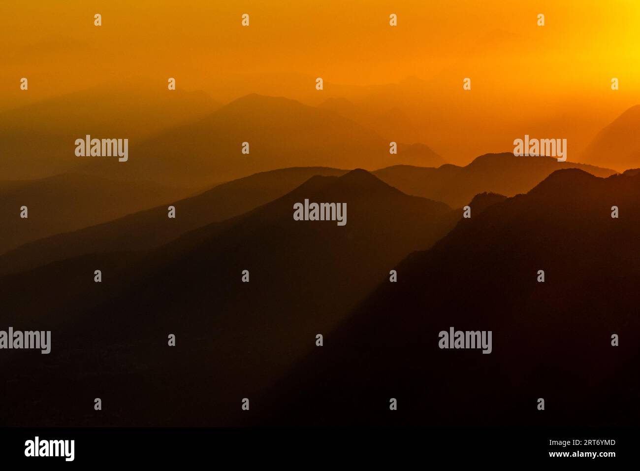Vue pittoresque silhouette de paysage brumeux d'énormes montagnes rocheuses sous le ciel de coucher du soleil avec des nuages orange dans la frontière du lac majeur entre l'Italie et Banque D'Images