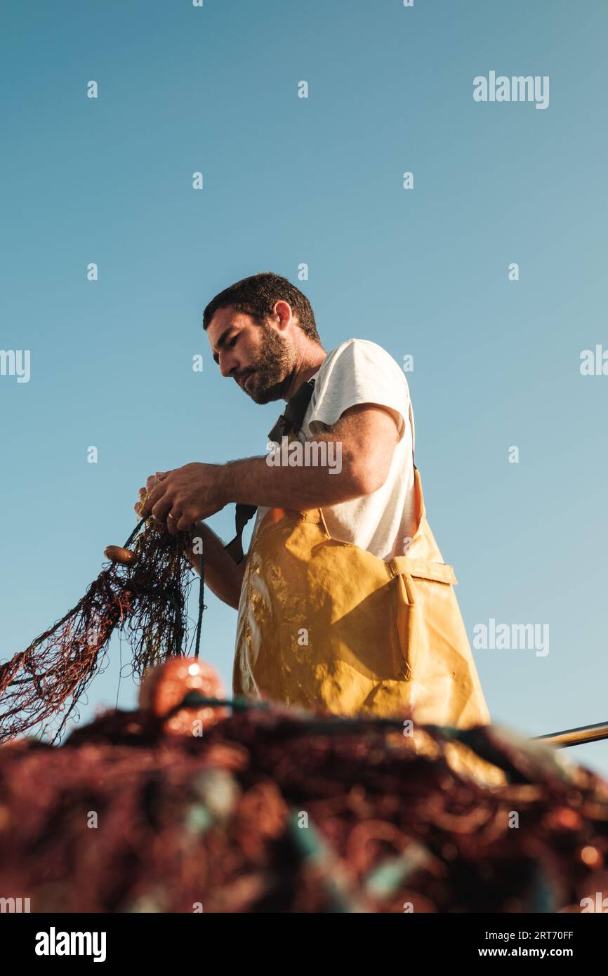 Doux foyer du pêcheur mâle barbu dans le tablier déliant le filet tandis que le senneur chasse le poisson sur chalutier à Soller près de l'île des Baléares de Majorque Banque D'Images