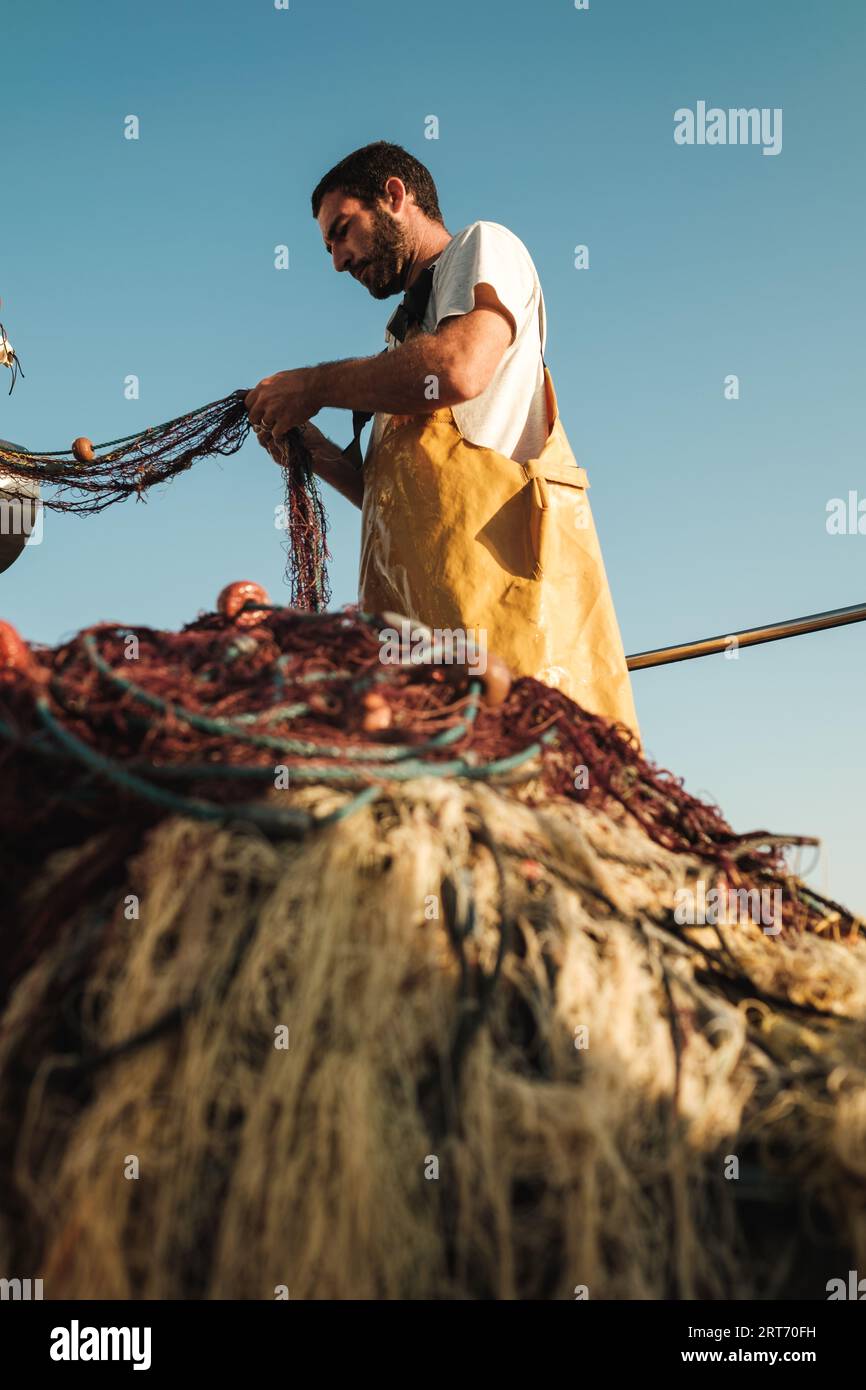 Doux foyer du pêcheur mâle barbu dans le tablier déliant le filet tandis que le senneur chasse le poisson sur chalutier à Soller près de l'île des Baléares de Majorque Banque D'Images