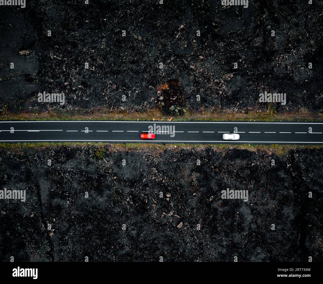 Route avec deux voitures avec flou de mouvement d'en haut par drone - photo de nuit à Lanzarote. Route droite parmi les laves sur les côtés dans les îles Canaries Banque D'Images
