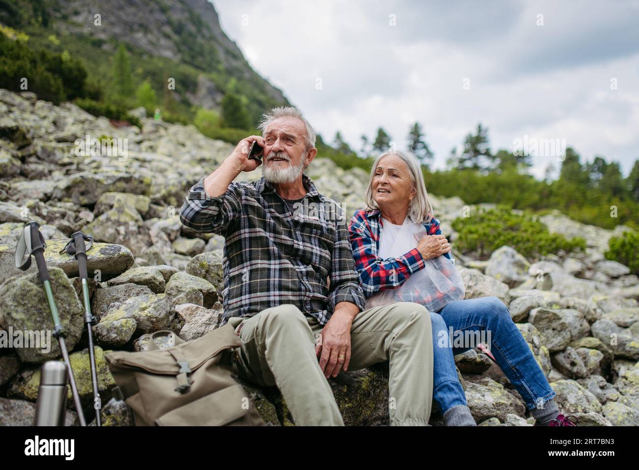 Touristes seniors assis sur des rochers et regardant la nature lointaine à travers des jumelles. Banque D'Images
