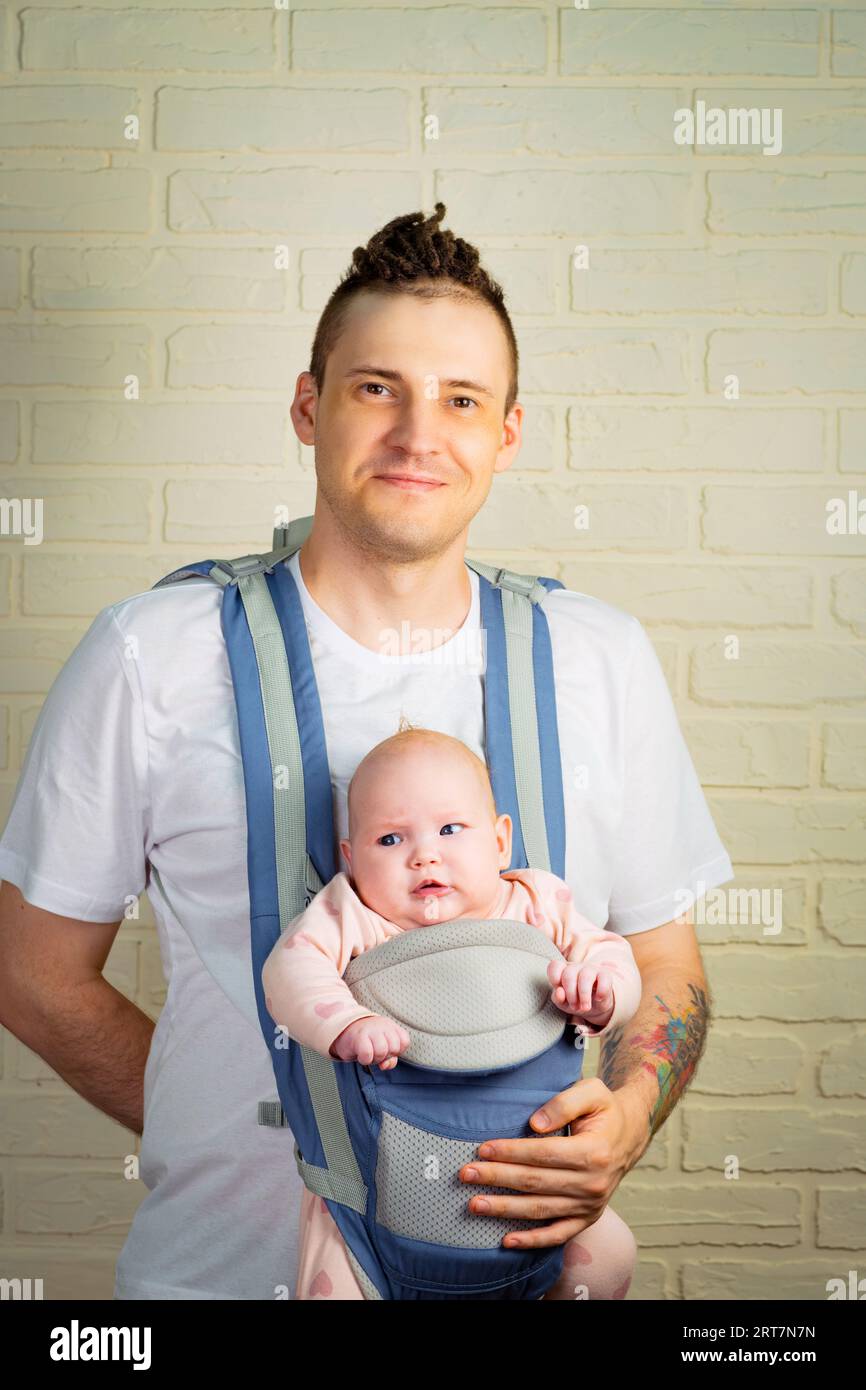 jeune père avec son bébé nouveau-né dans une écharpe, sur un fond de mur de briques Banque D'Images