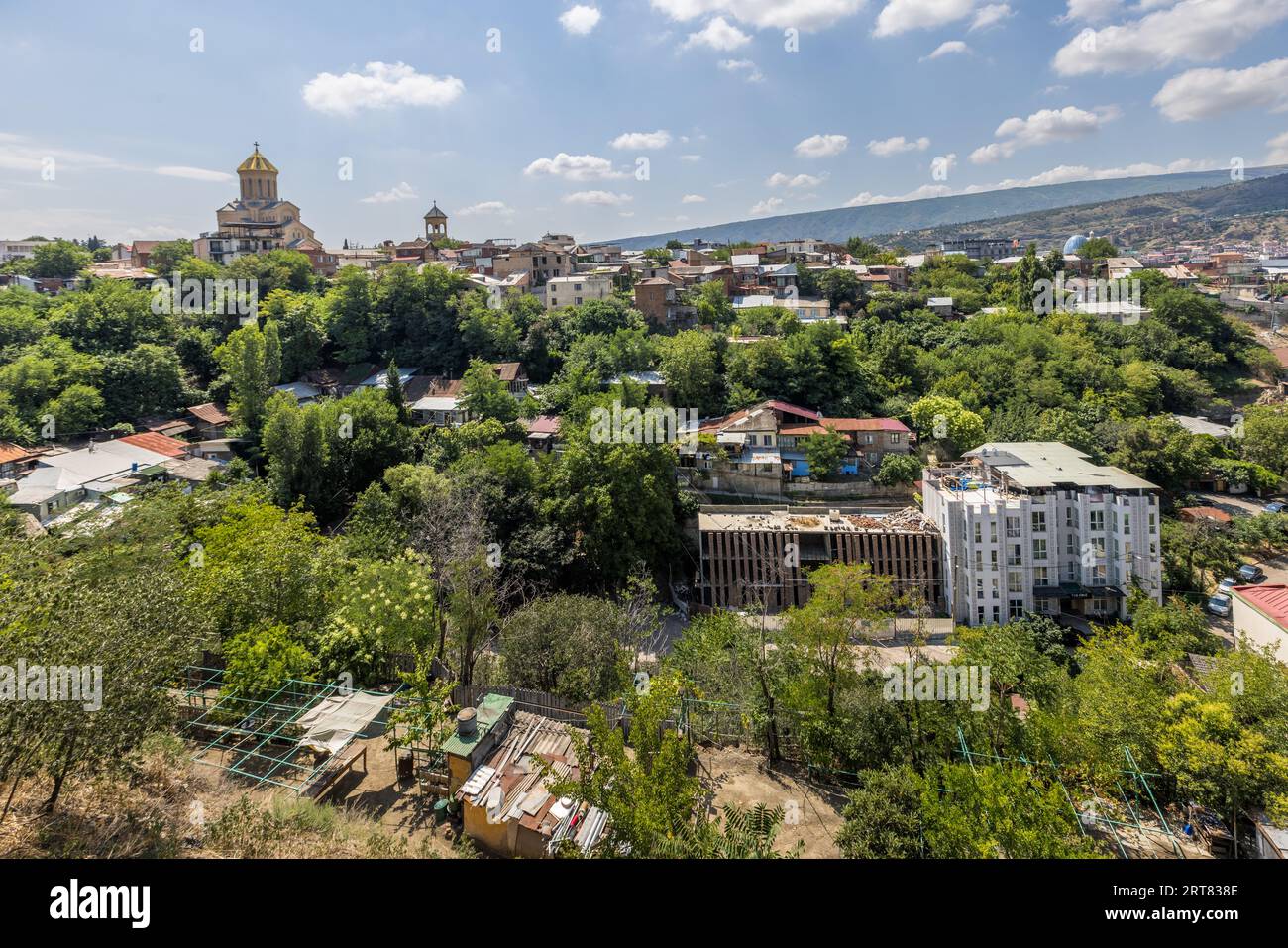 Vue du quartier de Chugureti à Tbilissi, Géorgie. La cathédrale de la Sainte Trinité avec son dôme doré se dresse sur une colline. Les bâtiments résidentiels et les arbres sont visibles. En arrière-plan se trouvent les montagnes Banque D'Images