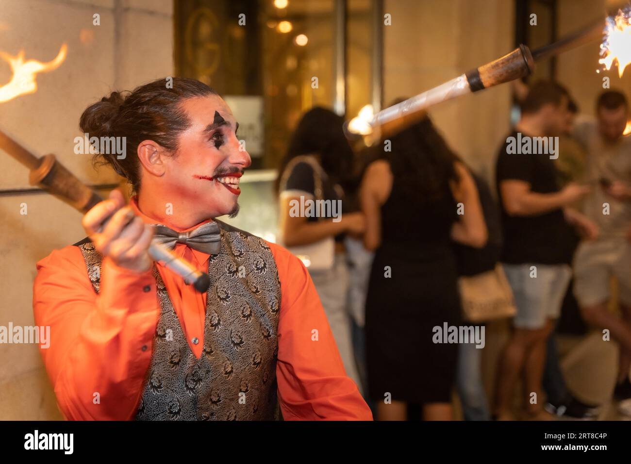 Jongleur souriant à une fête d'halloween jonglant des bâtons avec du feu, à l'entrée de la discothèque Banque D'Images