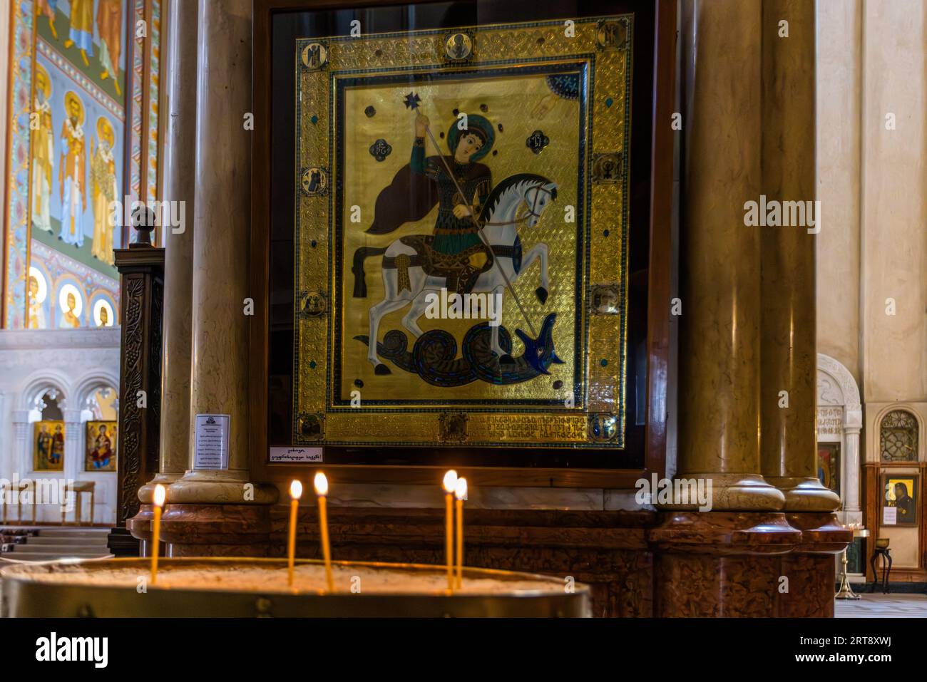 Une icône de Saint Georges est suspendue dans la cathédrale Sameba (cathédrale de la Sainte Trinité, Tsminda Sameba) à Tbilissi, en Géorgie. Elle représente le saint sur un cheval blanc, tuant un dragon avec sa lance. Un large cadre doré serti de pierres entoure l'image. Des bougies brûlent dans un bac à sable devant elle. Saint Georges est le saint patron du pays. La cathédrale a été construite de 1995 à 2004 sur la colline d'Élia dans le quartier d'Avlabari. Elle est l'église principale de l'Église orthodoxe géorgienne. Avec ses 86,1 mètres jusqu'au sommet de sa croix, c'est l'une des plus hautes cathédrales orthodoxes du monde. Banque D'Images