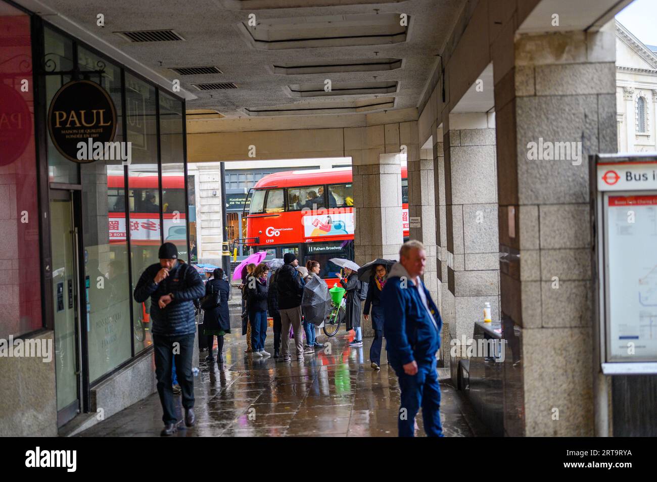 LONDRES - 24 avril 2023 : les Londoniens cherchent un abri de la pluie près de la gare de Charing Cross, avec l'emblématique bus à impériale rouge londonien dans le Banque D'Images
