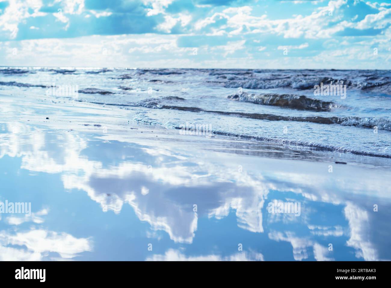 Vue fabuleuse de l'eau douce miroir de la côte de bord de mer près des vagues reflétant le ciel bleu, nuages blancs sur la journée ensoleillée. Été, vacances, vacances, Banque D'Images