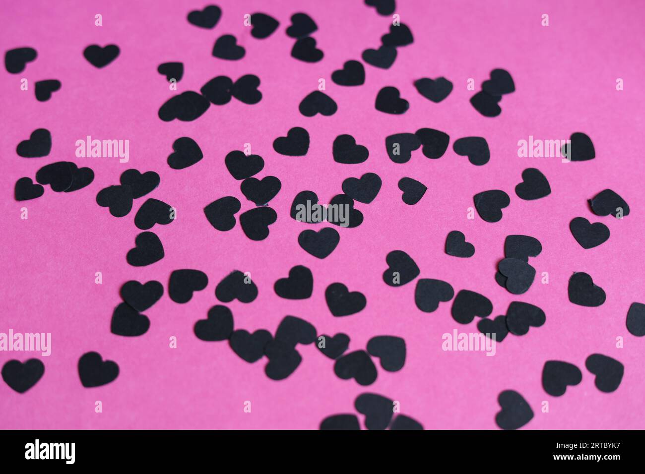 confettis de papier en forme de coeur noir sur un fond de papier rose Banque D'Images