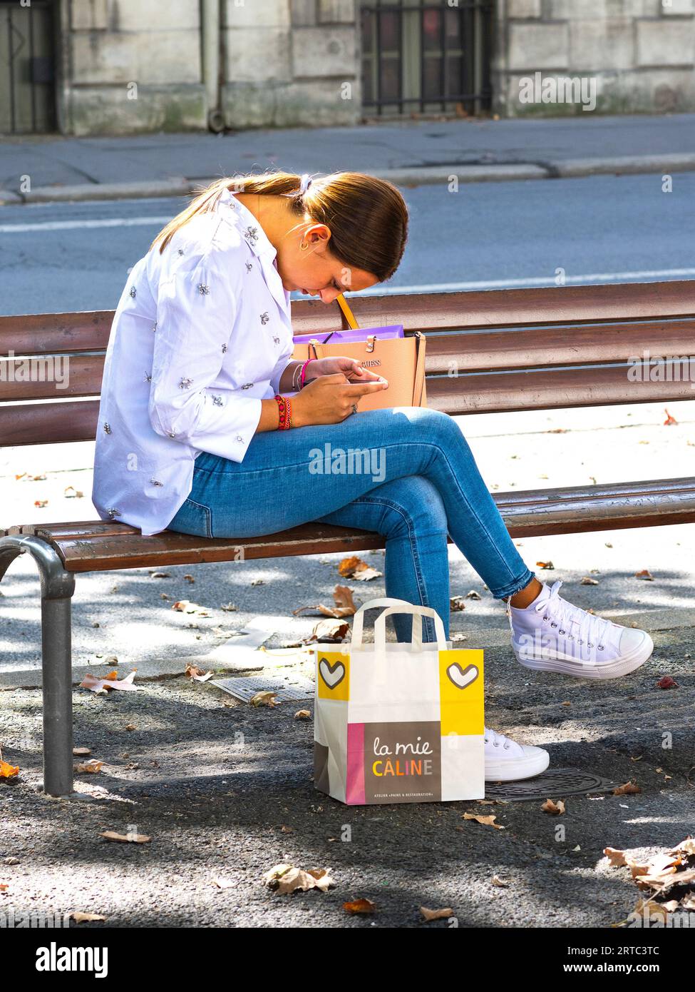 Jeune femme habillée de façon décontractée assise sur un banc du centre-ville, étudiant smartphone - Tours, Indre-et-Loire (37), France. Banque D'Images