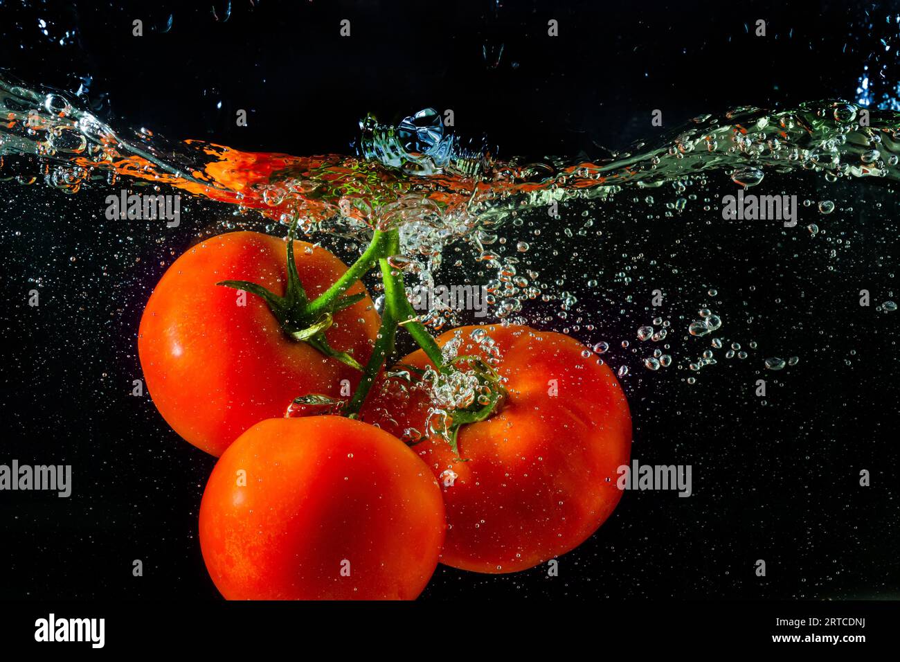 Tomate rouge fraîche tombant dans l'eau avec des éclaboussures d'eau et des bulles d'air isolées sur fond noir. Banque D'Images