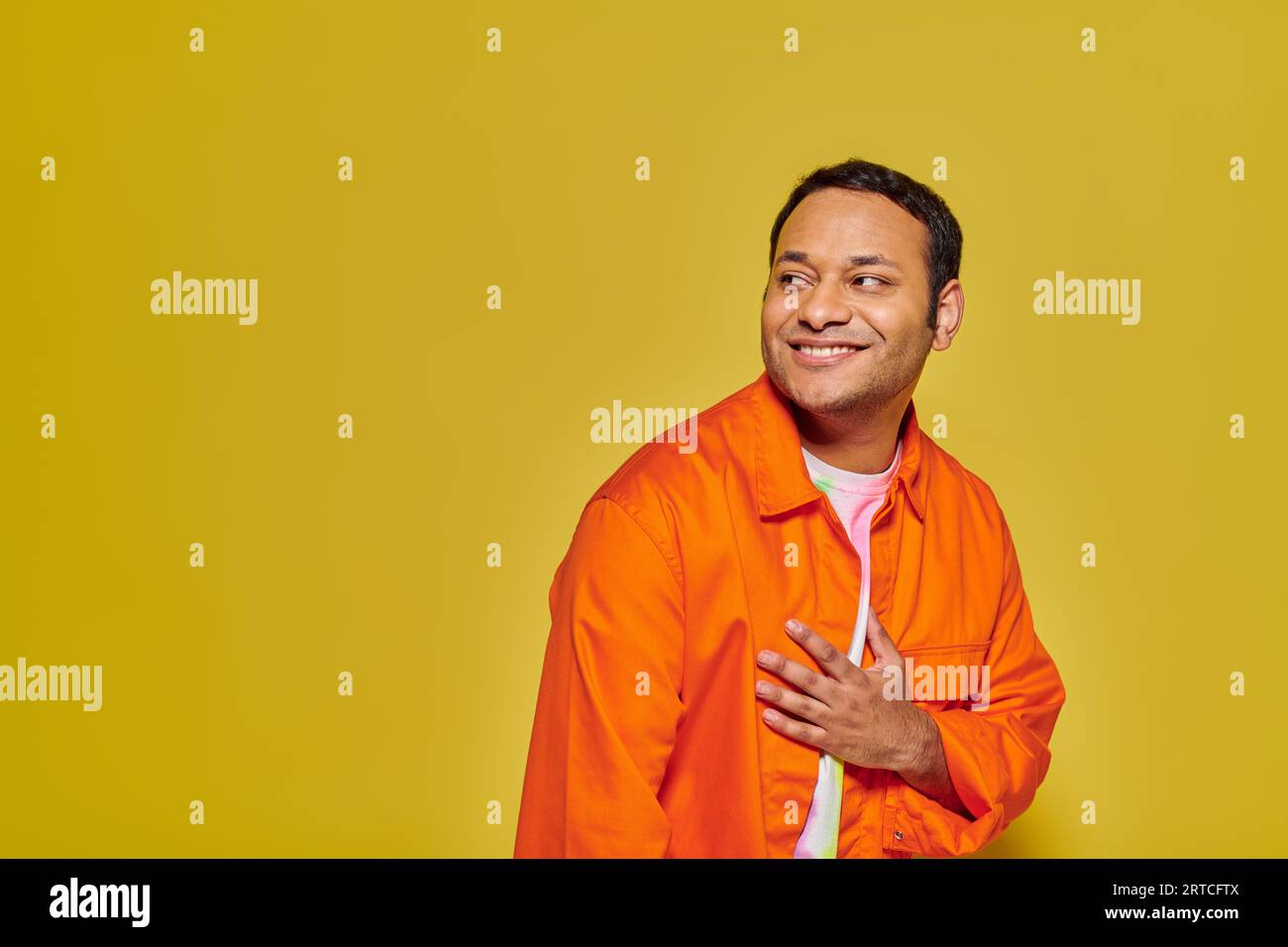 portrait d'homme indien positif dans la veste orange regardant loin et souriant sur fond jaune Banque D'Images