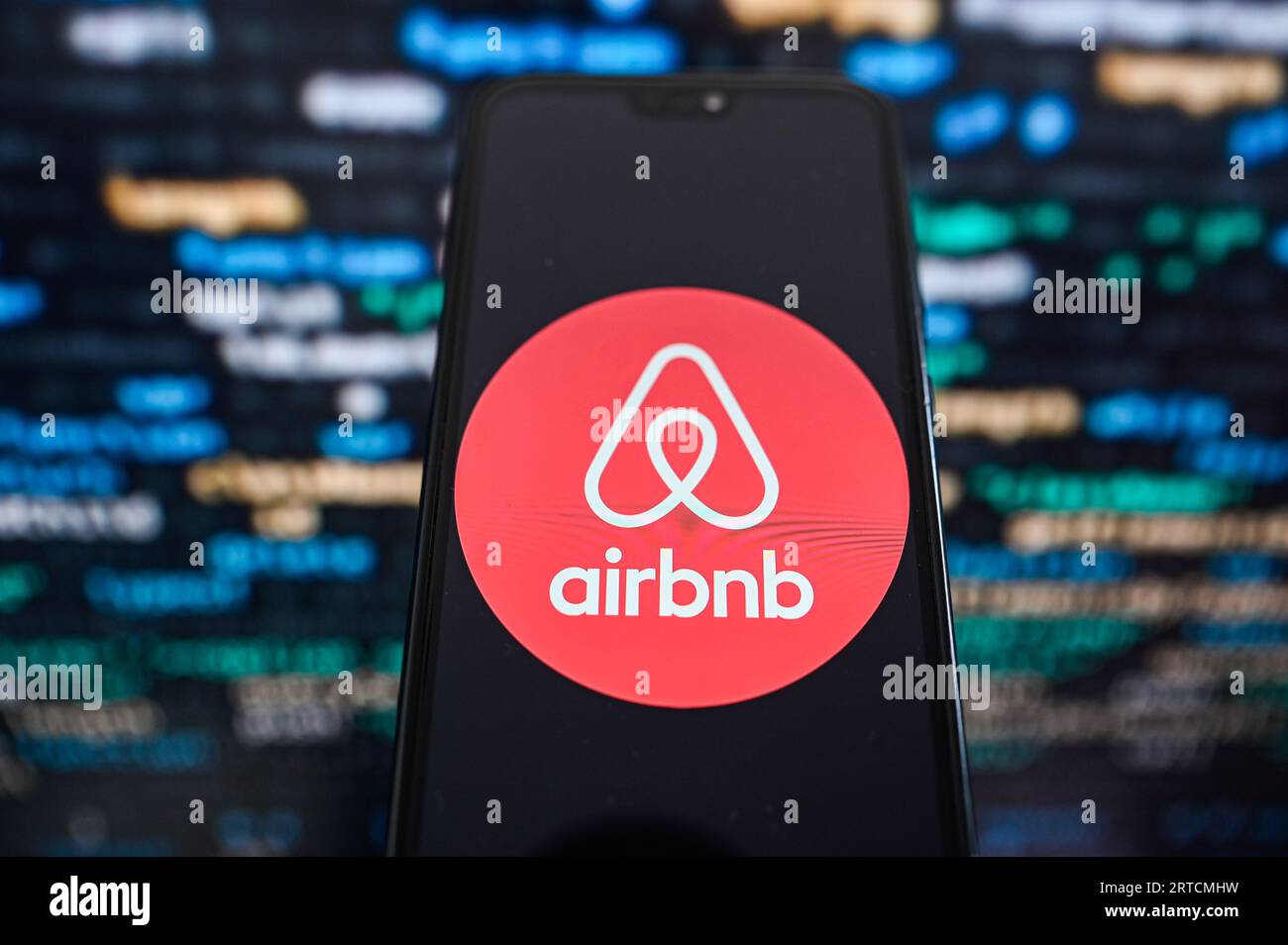 Dans cette illustration photo, un logo Airbnb affiché sur un smartphone avec code de programmation en arrière-plan. Banque D'Images