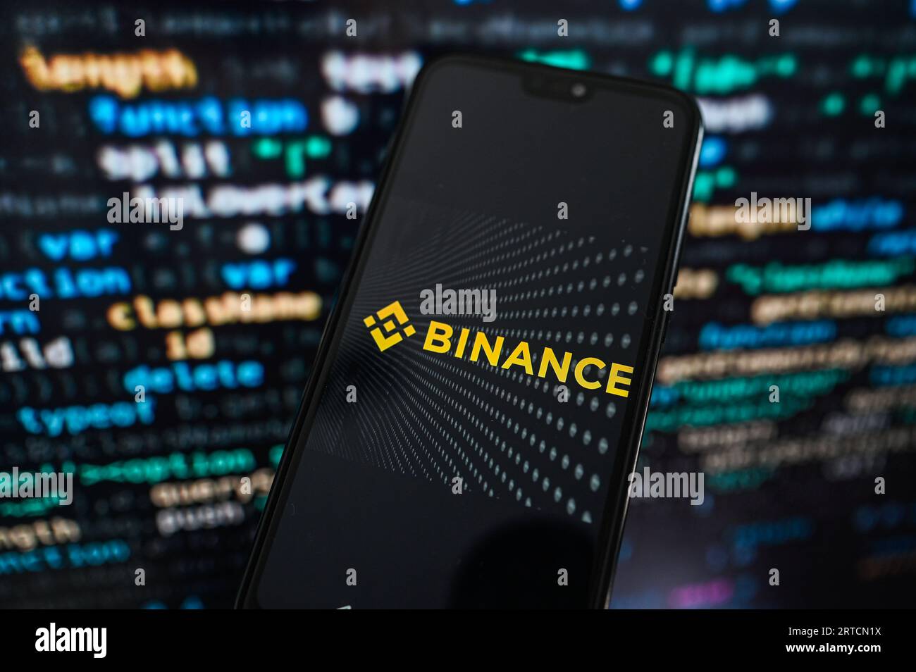 Sur cette photo, un logo Binance affiché sur un smartphone avec un code de programmation sur le fond. Banque D'Images