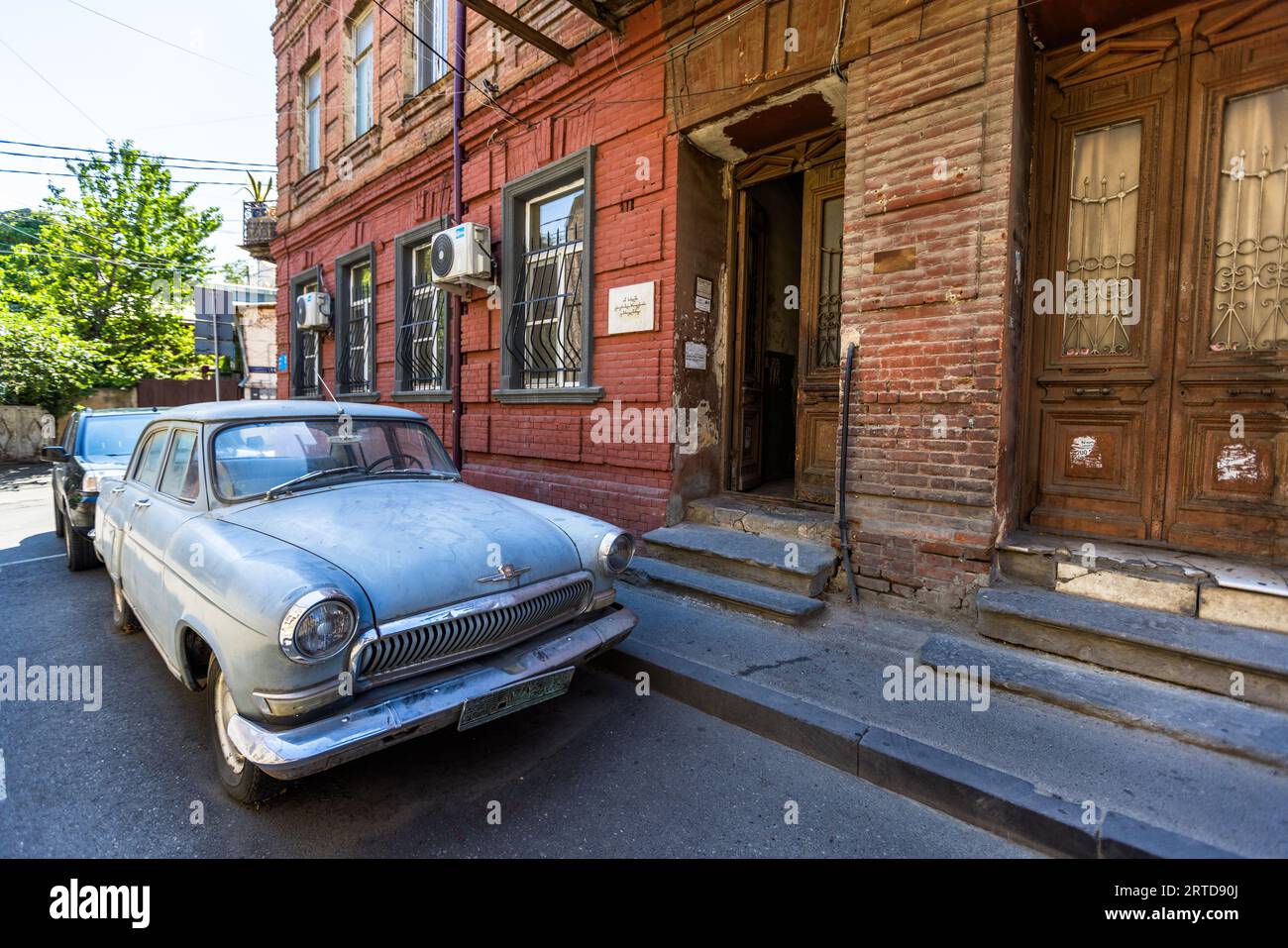 Une voiture vintage bleu clair est garée devant un bâtiment en briques rouges à Tbilissi. Le bâtiment a des fenêtres et une porte en bois. L'endroit est Mtatsminda, Géorgie Banque D'Images