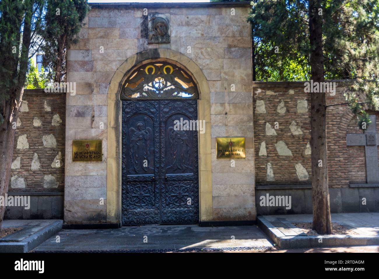 Entrée au Patriarcat de Géorgie. Une porte métallique avec des reliefs est sertie dans un mur de pierre. Deux signes dorés sont attachés au mur. Tbilissi, Géorgie Banque D'Images
