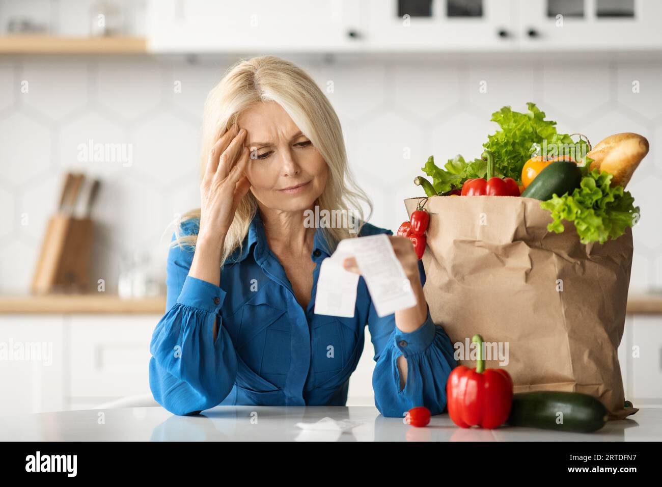 Dépenses d'épicerie. Dame principale stressée dans la cuisine vérifiant la facture après avoir fait des achats de nourriture Banque D'Images