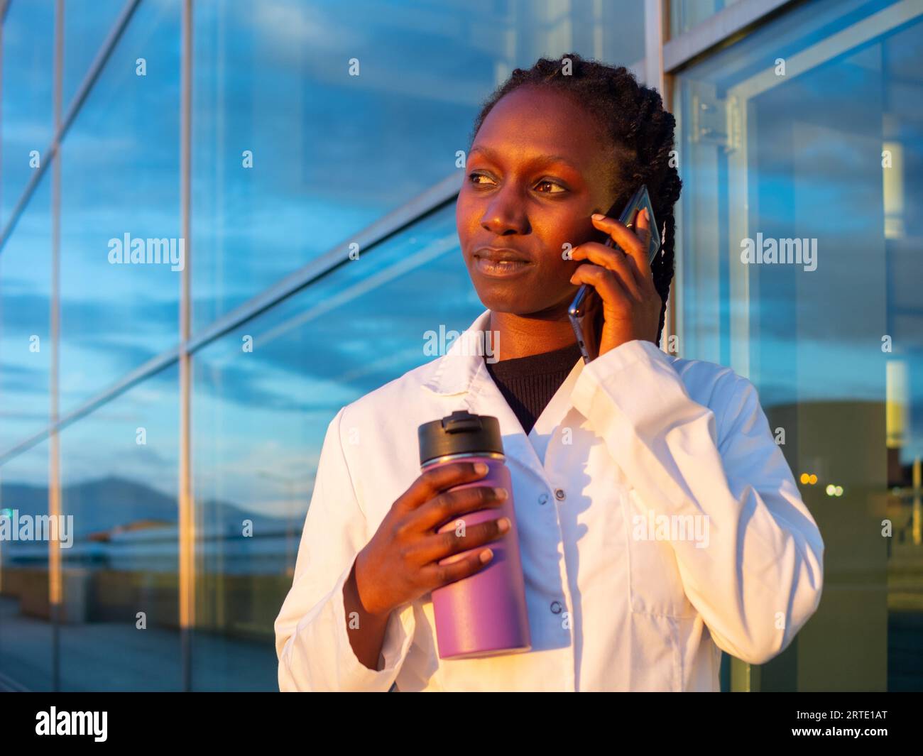 jeune femme médecin parlant par téléphone tout en tenant un café thermo devant un hôpital Banque D'Images
