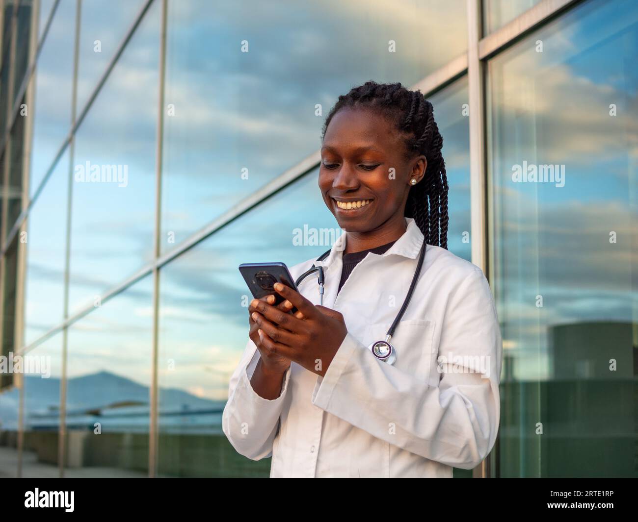 Jeune femme médecin vérifiant et tapant sur son téléphone devant un hôpital Banque D'Images