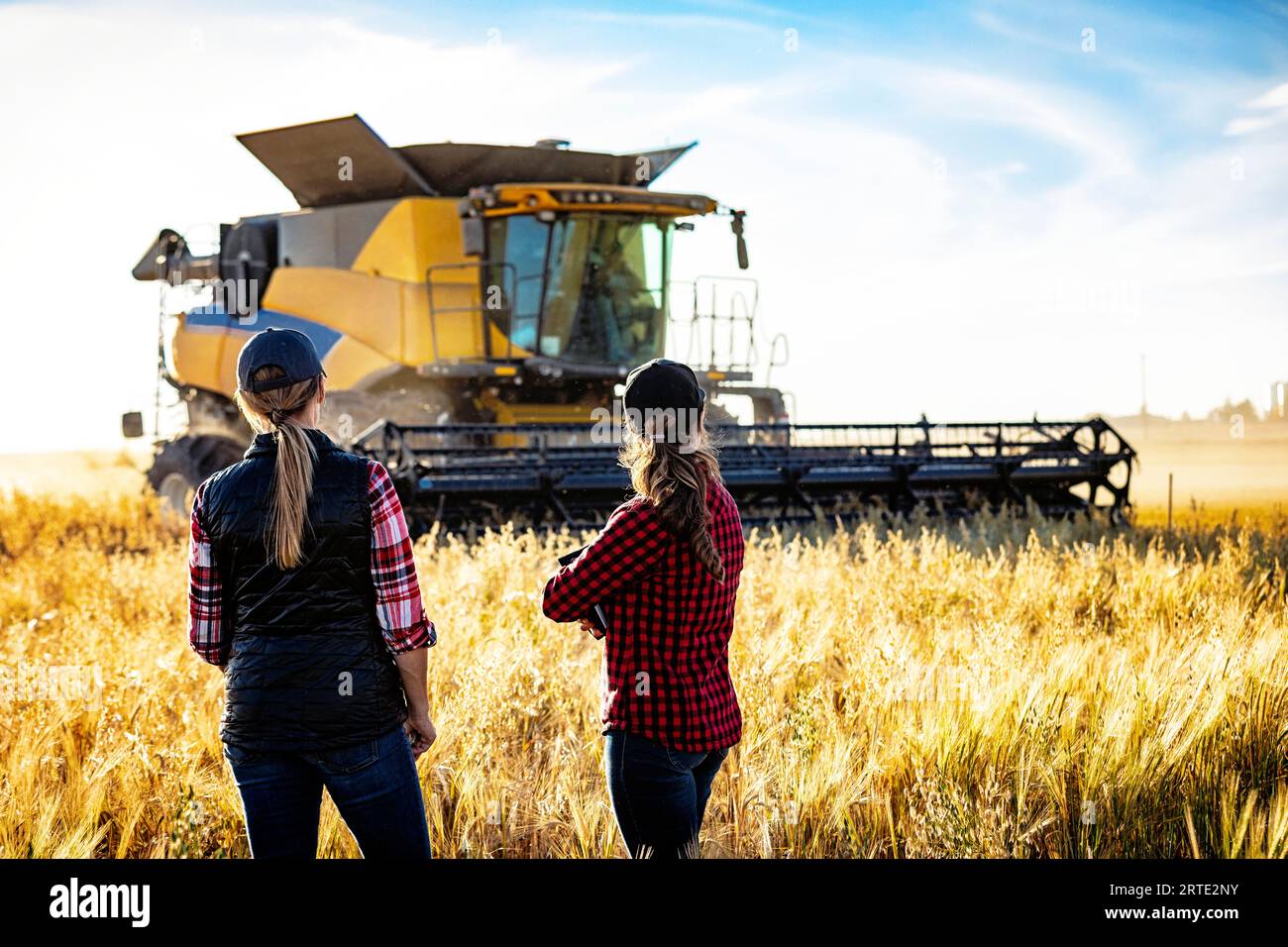 Vue prise de derrière d'une femme agricole mature debout dans un champ travaillant avec une jeune femme au moment de la récolte, en utilisant Advanced Agricultural ... Banque D'Images