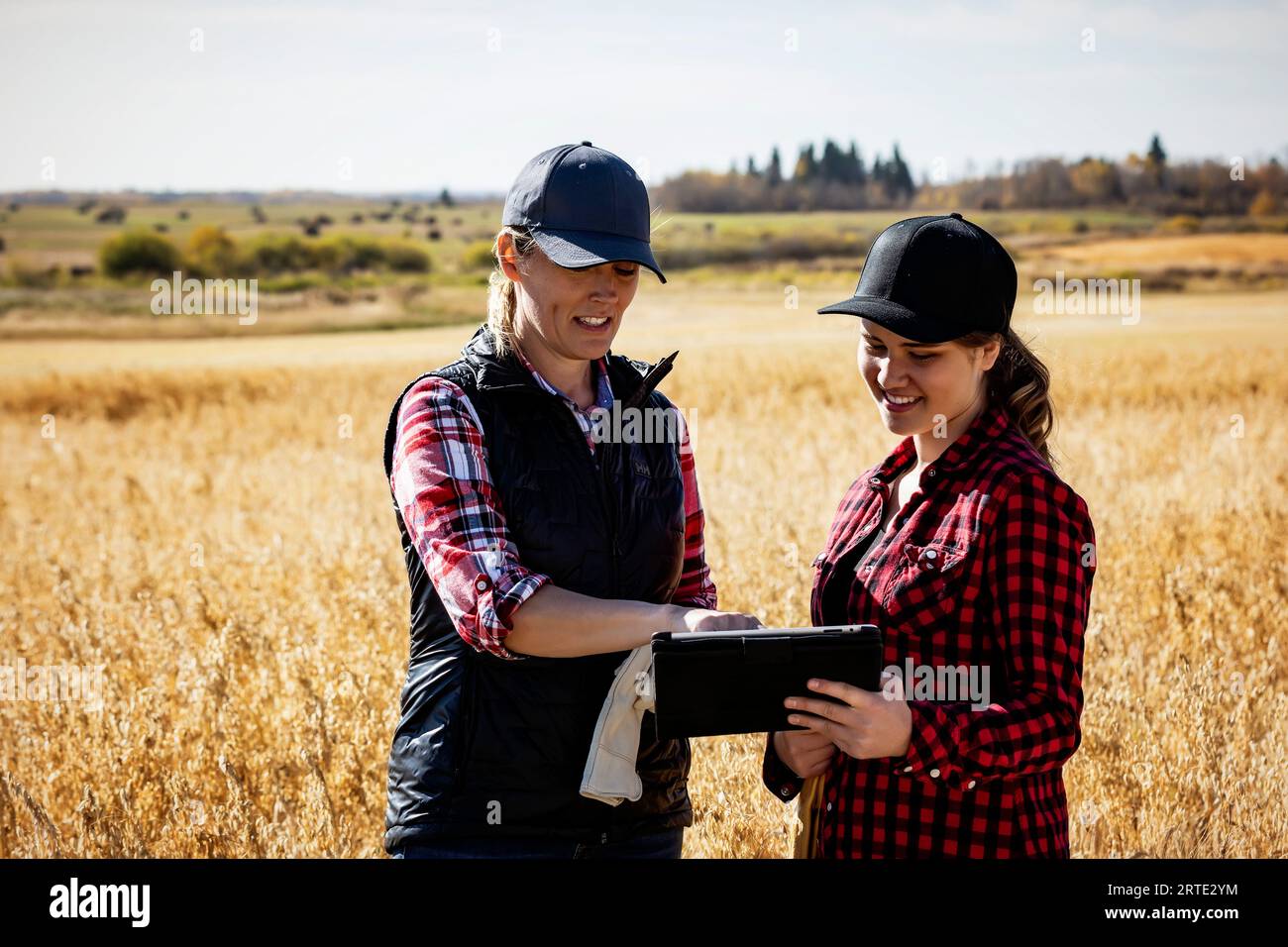Une femme agricole mature debout dans un champ travaillant avec une jeune femme au moment de la récolte, en utilisant une technologie de logiciel agricole avancée sur un tapis Banque D'Images