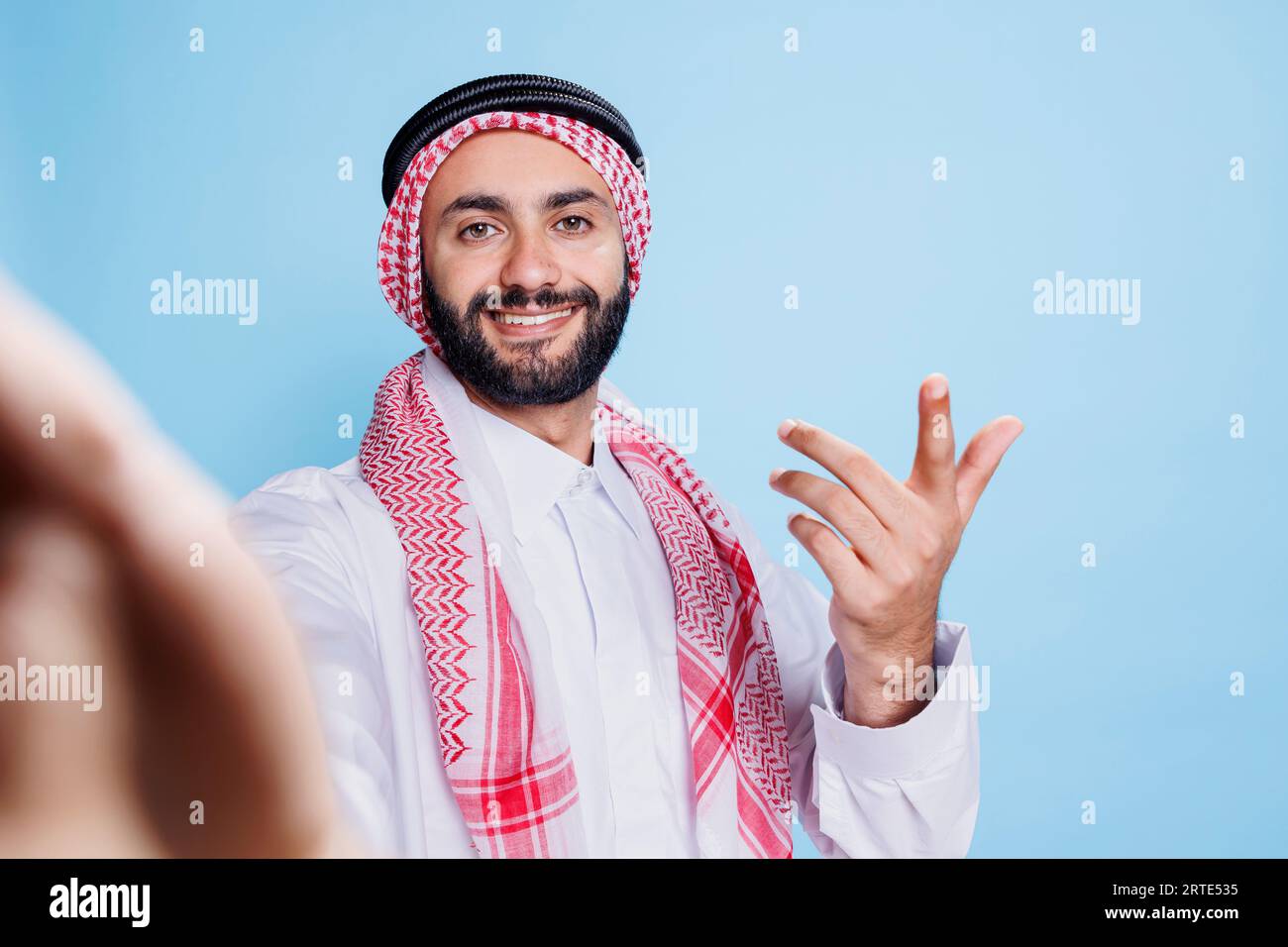 Homme musulman joyeux portant des vêtements traditionnels s'engageant dans un appel vidéo du point de vue de pov. Personne arabe souriante dans thobe et foulard regardant la caméra avant tout en parlant dans une réunion en ligne Banque D'Images