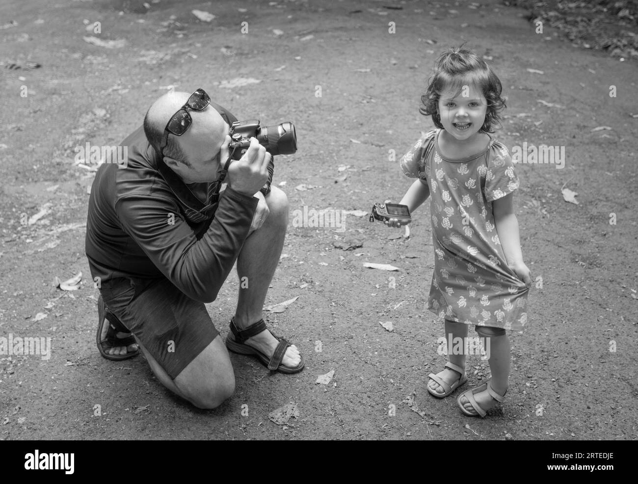 Père se penchant pour photographier sa fille alors qu'elle regarde vers l'avant et sourit à la caméra, Road to Hana ; Maui, Hawaii, États-Unis d'Amérique Banque D'Images
