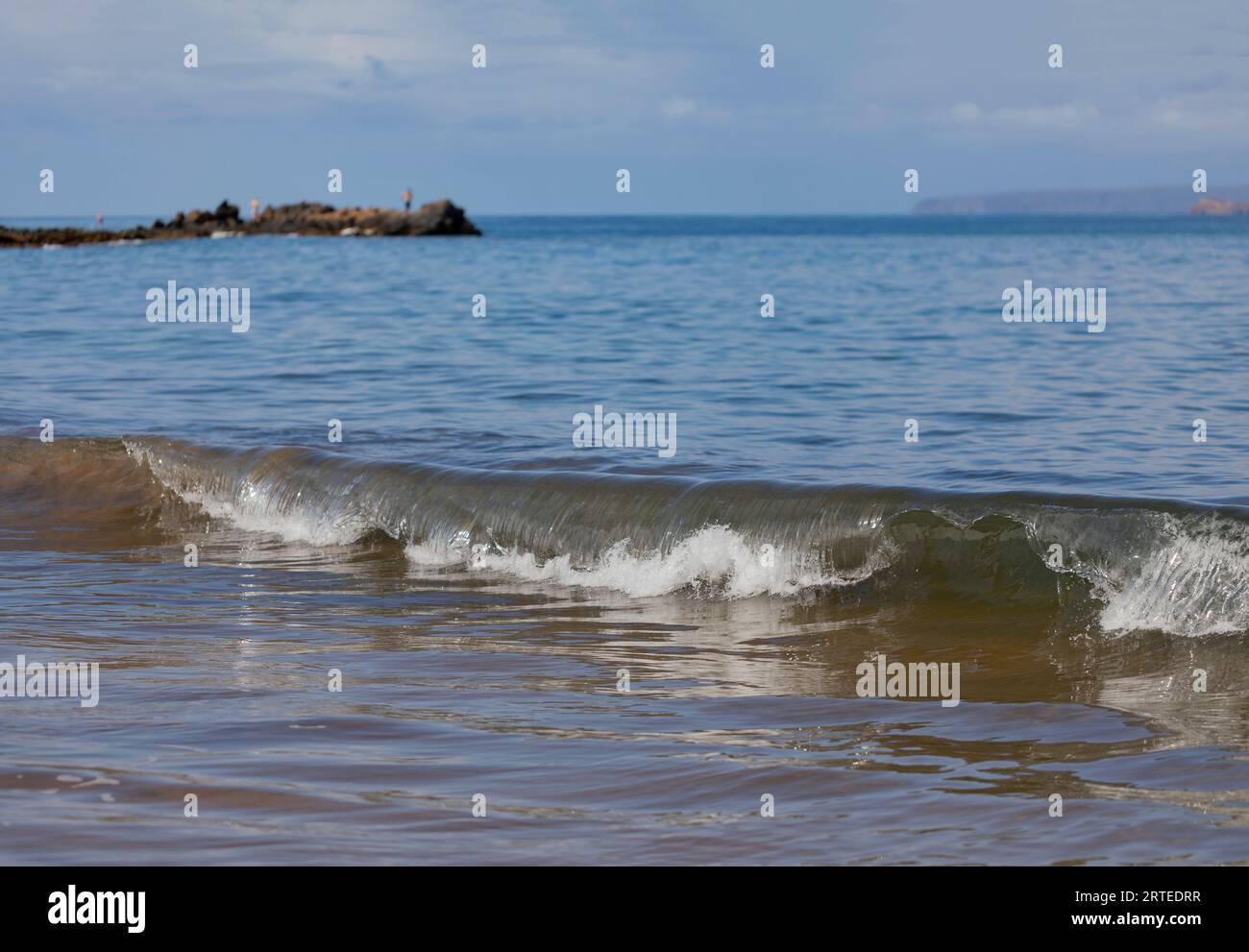 Roulant, vague de l'océan s'élevant le long de la rive de Kamaole 2 Beach avec des gens debout sur un promontoire rocheux regardant dans l'océan Pacifique dans le di... Banque D'Images