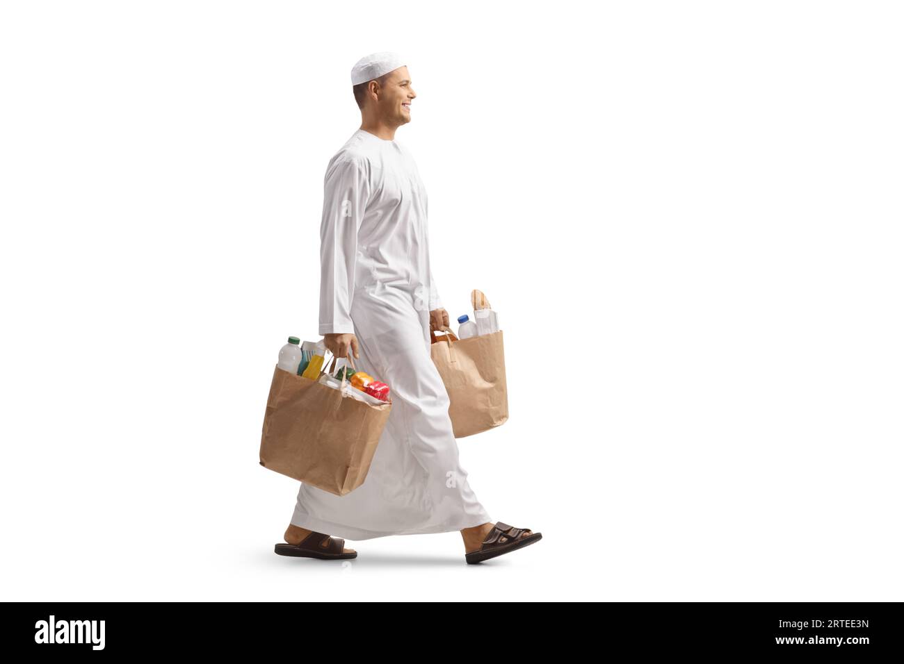 Photo de profil pleine longueur d'un homme en vêtements ethniques marchant et portant des sacs d'épicerie isolé sur fond blanc Banque D'Images