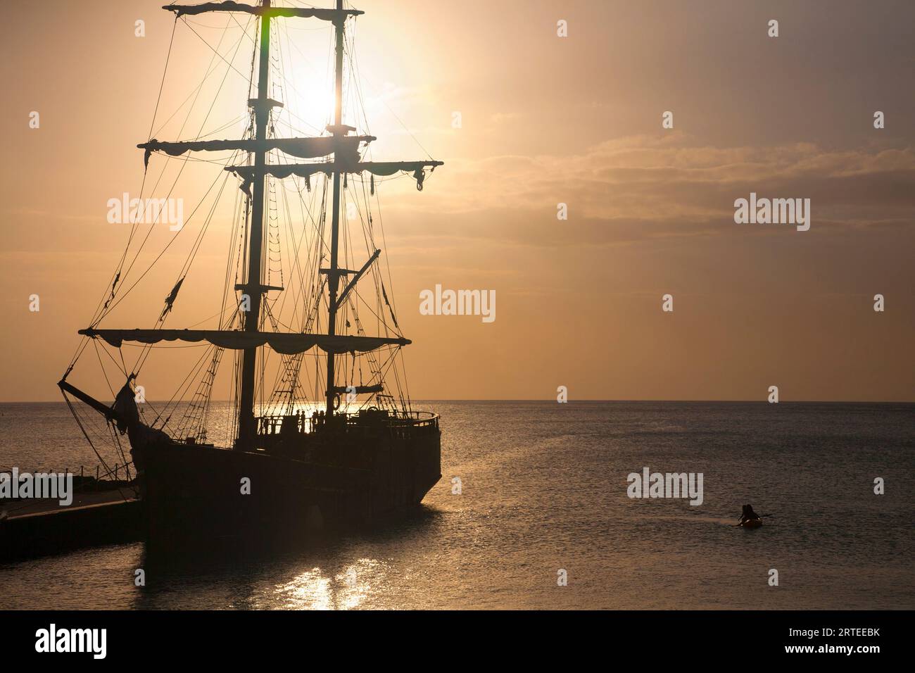 Silhouette de personnes à bord d'un grand voilier amarré au quai dans la capitale des îles Caïmans, George Town avec des kayakistes le long du côté pagayant dehors... Banque D'Images