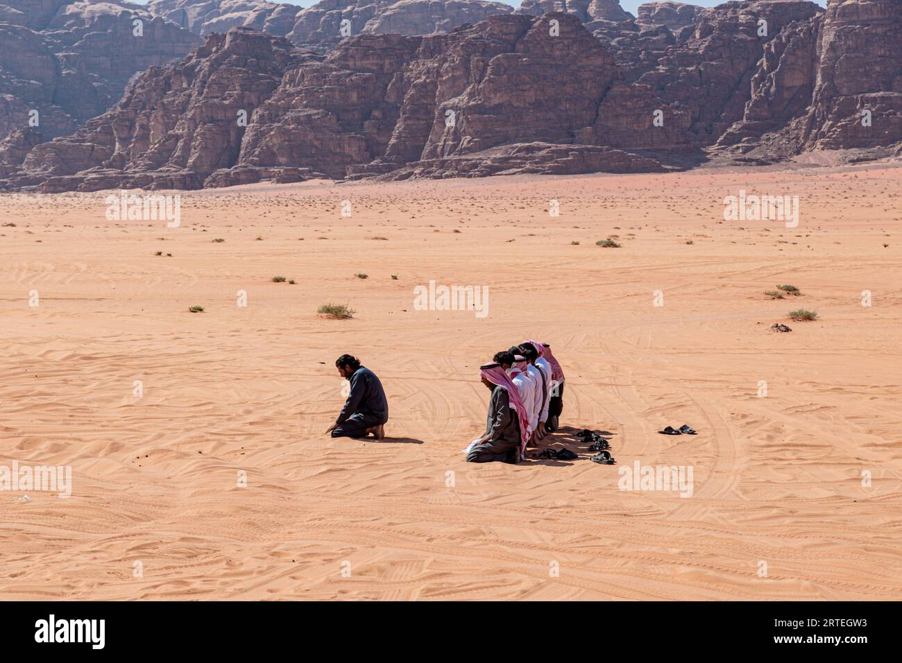 Des hommes bédouins se prosternant pour la prière musulmane au milieu du désert de Wadi Rum, en Jordanie Banque D'Images