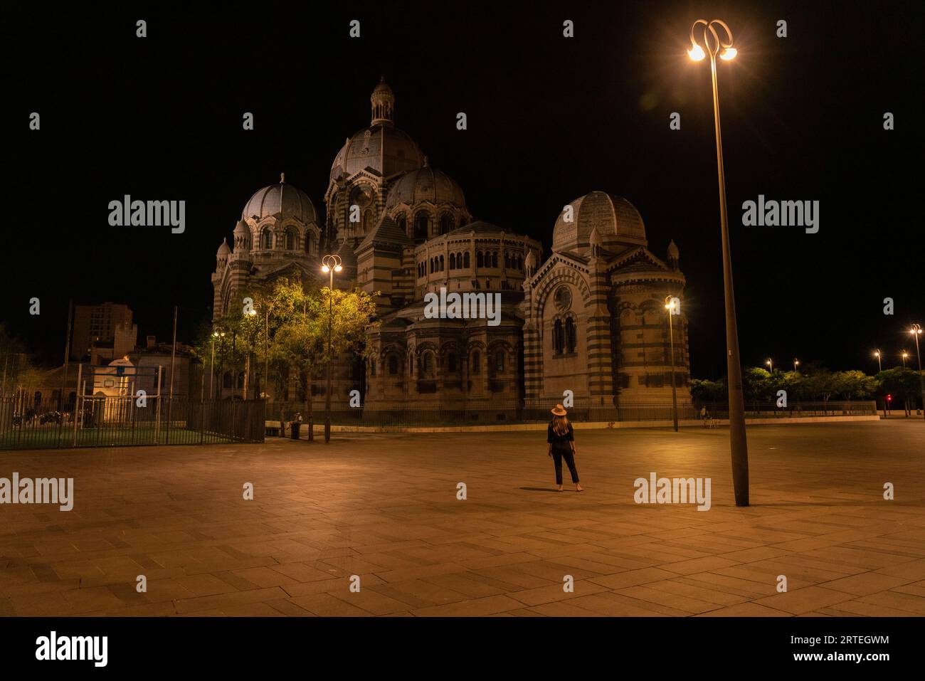 Femme se tient debout admirant la cathédrale de Marseille la nuit, avec un lampadaire brillant dans l'obscurité ; Marseille, France Banque D'Images
