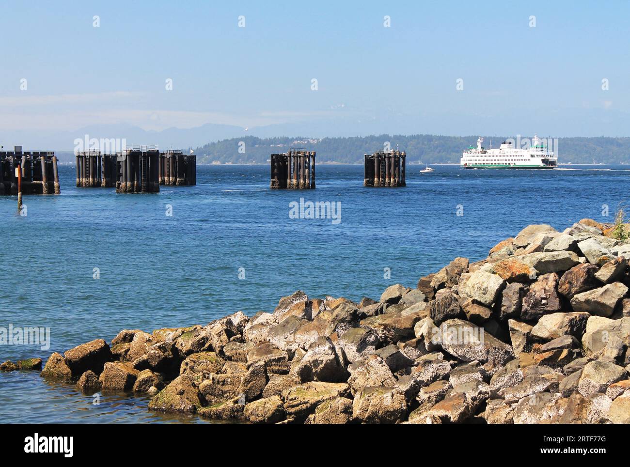 Avec une jetée rocheuse au premier plan, un emblématique ferry blanc de l'État de Washington s'éloigne de la jetée d'Edmonds, Washington, sur son chemin à travers Puget Sound Banque D'Images