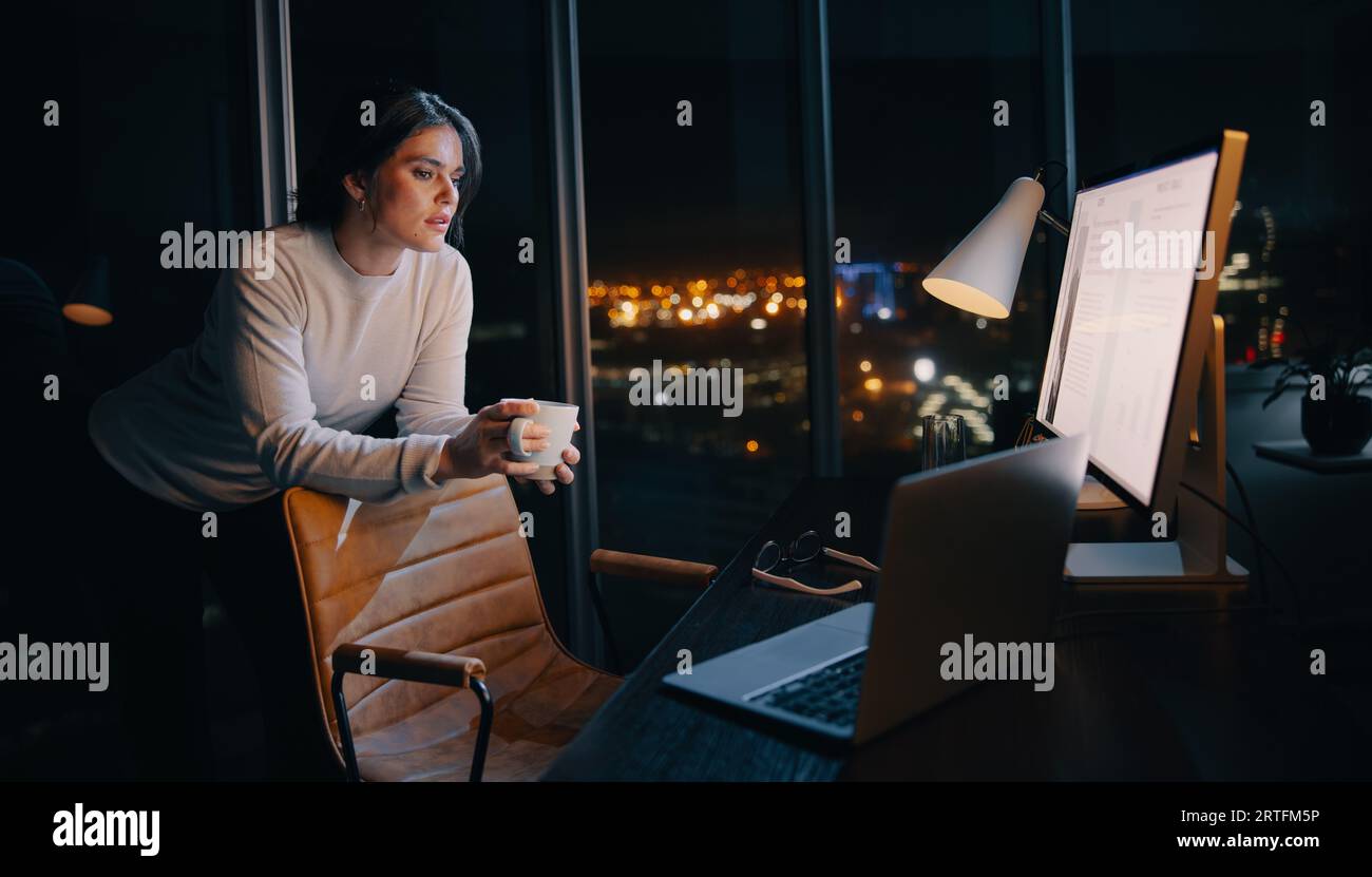 Femme d'affaires réfléchie travaille tard dans la nuit dans son bureau à domicile, concentrée sur un projet de marketing numérique. Femme professionnelle travaillant avec un ordinateur an Banque D'Images