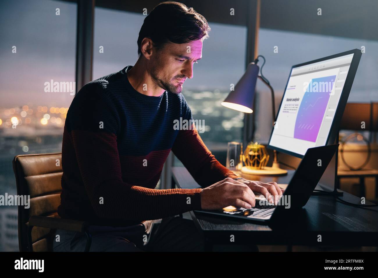 Homme d'affaires caucasien assis à son bureau dans un bureau la nuit, utilisant un ordinateur portable pour l'analyse et la recherche de marché. Homme professionnel travaillant tard, Ty Banque D'Images