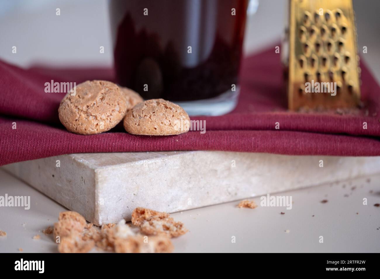 Biscuits Amaretto à côté d'une tasse à café en verre sur une serviette rouge et plateau en marbre Une petite râpe dorée en arrière-plan. Photo de haute qualité. Banque D'Images