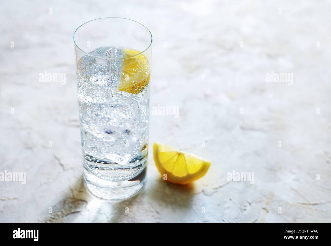 Eau minérale gazeuse fraîche avec des glaçons et des tranches de citron dans un verre à boire, boisson rafraîchissante sur un fond de pierre clair, espace de copie, sélectionné Banque D'Images