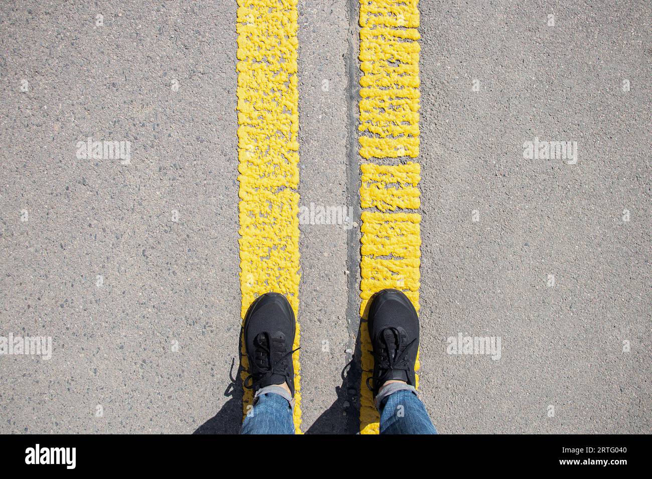 Les jambes féminines dans les baskets se tiennent sur deux bandes jaunes sur l'asphalte, pointant vers l'avant, la route devant, le chemin du succès Banque D'Images