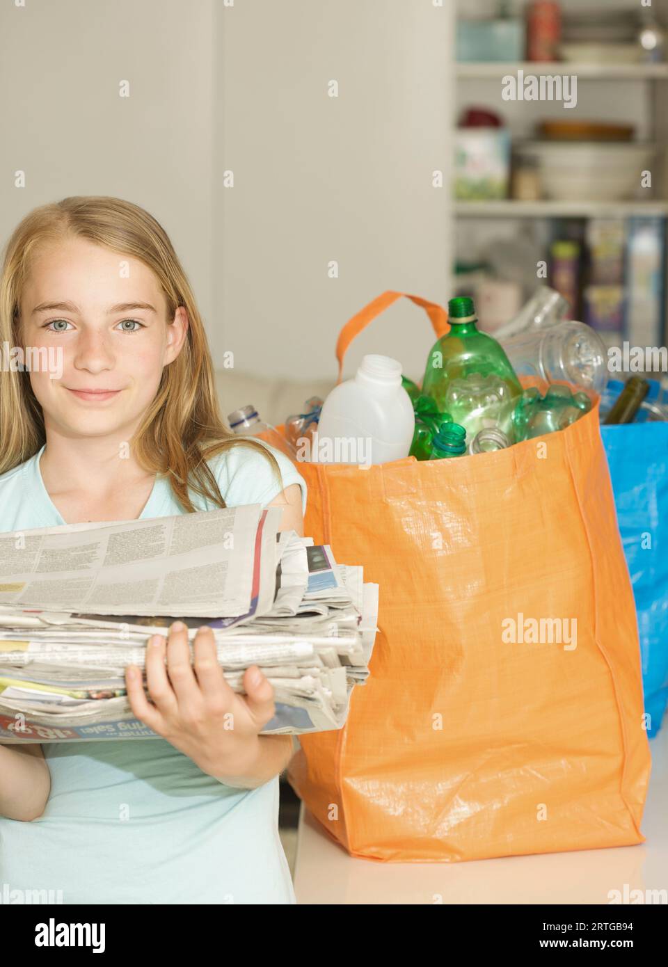 Jeune fille debout à côté de sacs de recyclage tenant une pile de journaux Banque D'Images