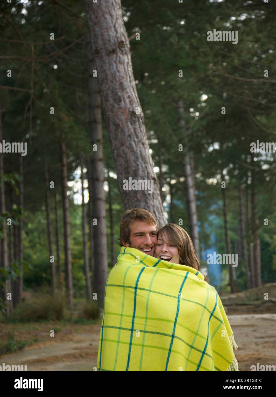 Jeune couple standing in a forest enveloppé dans une couverture de rire Banque D'Images