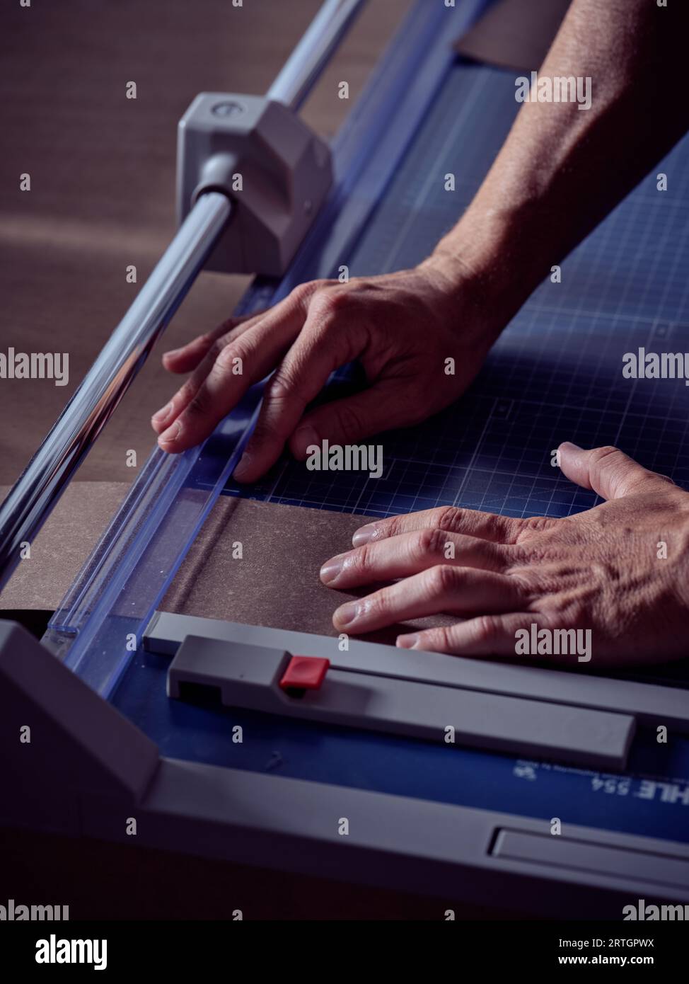 Angle élevé de l'artisan masculin anonyme utilisant la machine de découpe et travaillant avec le papier à l'établi dans l'atelier de reliure Banque D'Images