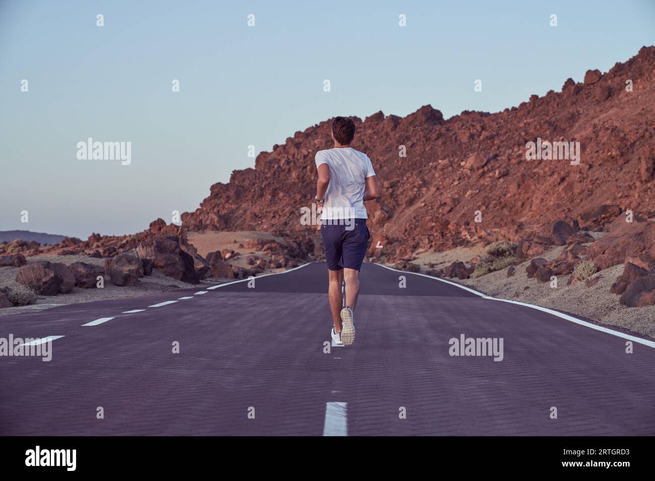 Vue arrière du corps entier du mâle actif anonyme courant sur l'autoroute asphaltée vide près de la crête de montagne dans la nature le jour d'été Banque D'Images