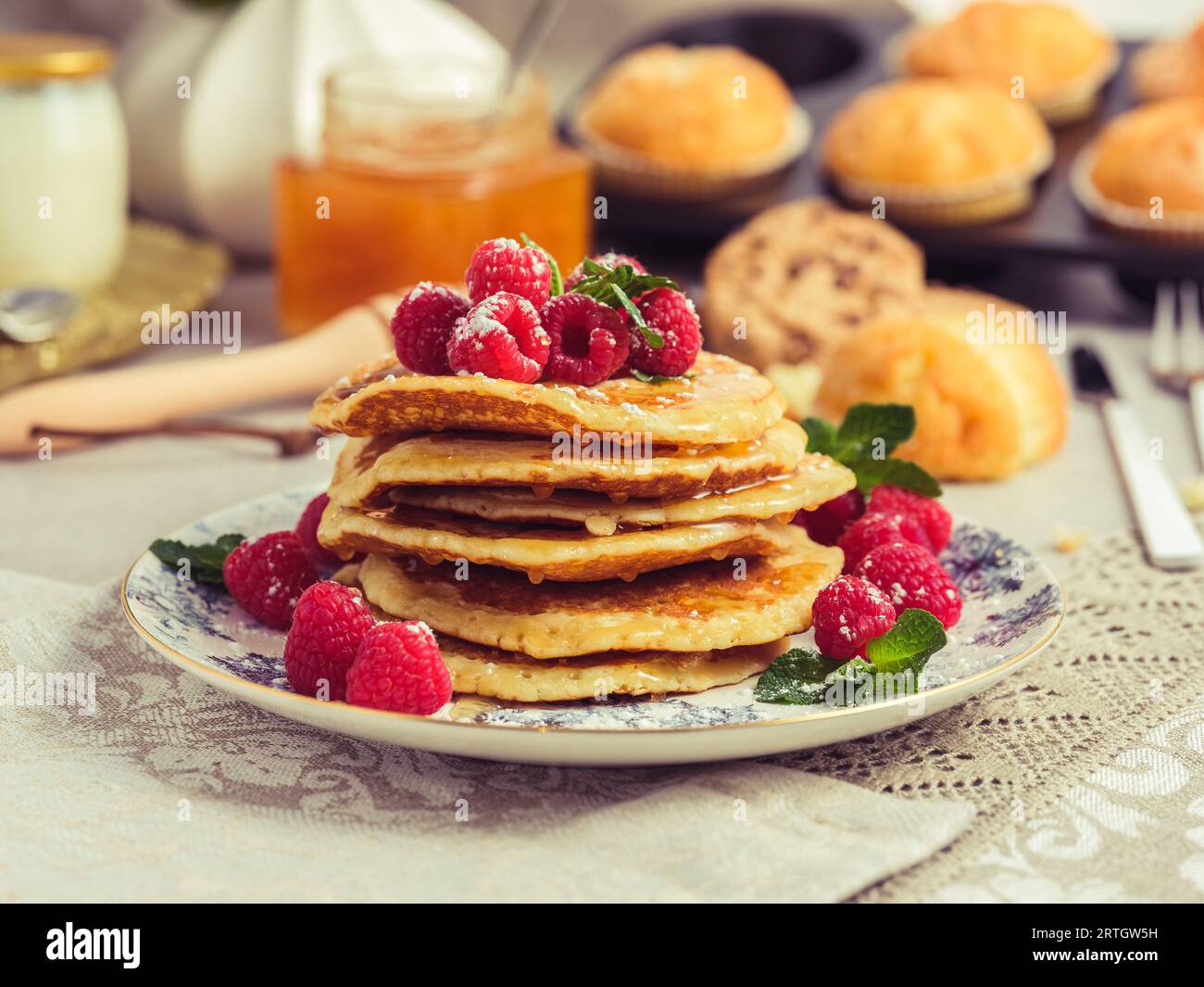 Pile de crêpes sucrées appétissantes servies sur assiette avec des framboises mûres et des feuilles de menthe pour le petit déjeuner à la maison Banque D'Images