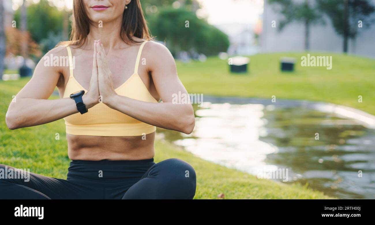 Portrait rogné de femme caucasienne heureuse exerçant le yoga à l'extérieur tôt le matin. Herbe verte dans le parc en été Banque D'Images