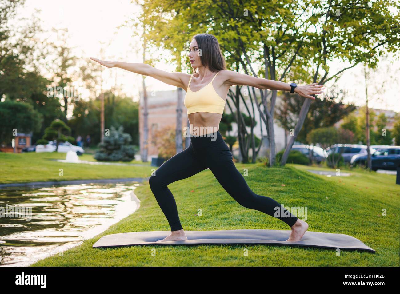 Vue latérale d'une jeune femme en forme s'exerçant sur un tapis dans le parc. Femme de fitness. Étirement sur tapis de fitness, concept de bien-être. Banque D'Images