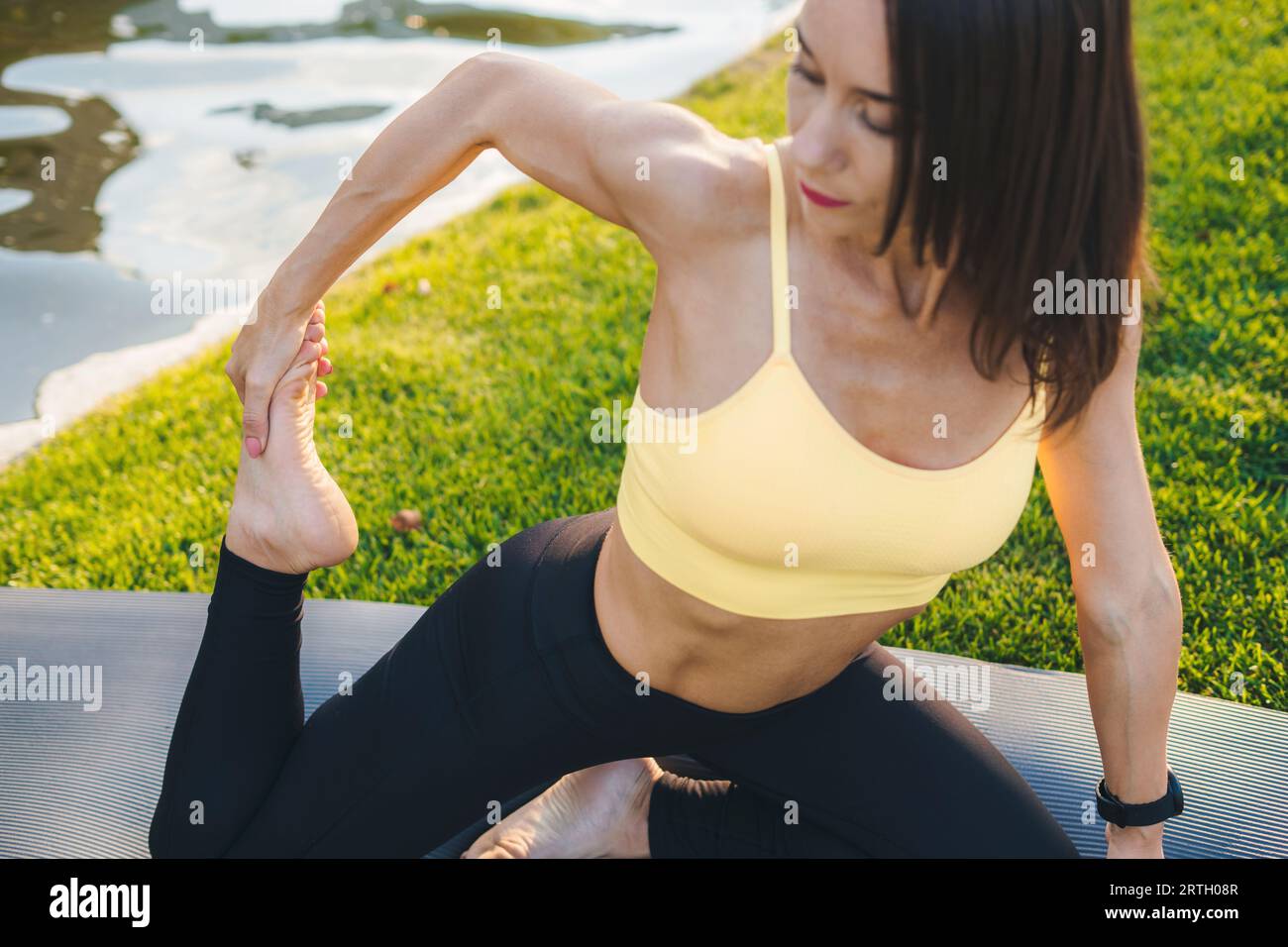 Femme adulte attrayante ayant un body strecching ajusté sur le tapis de yoga dans le parc vert, concept de loisirs de personnes et concept de soins de santé. Sain Banque D'Images
