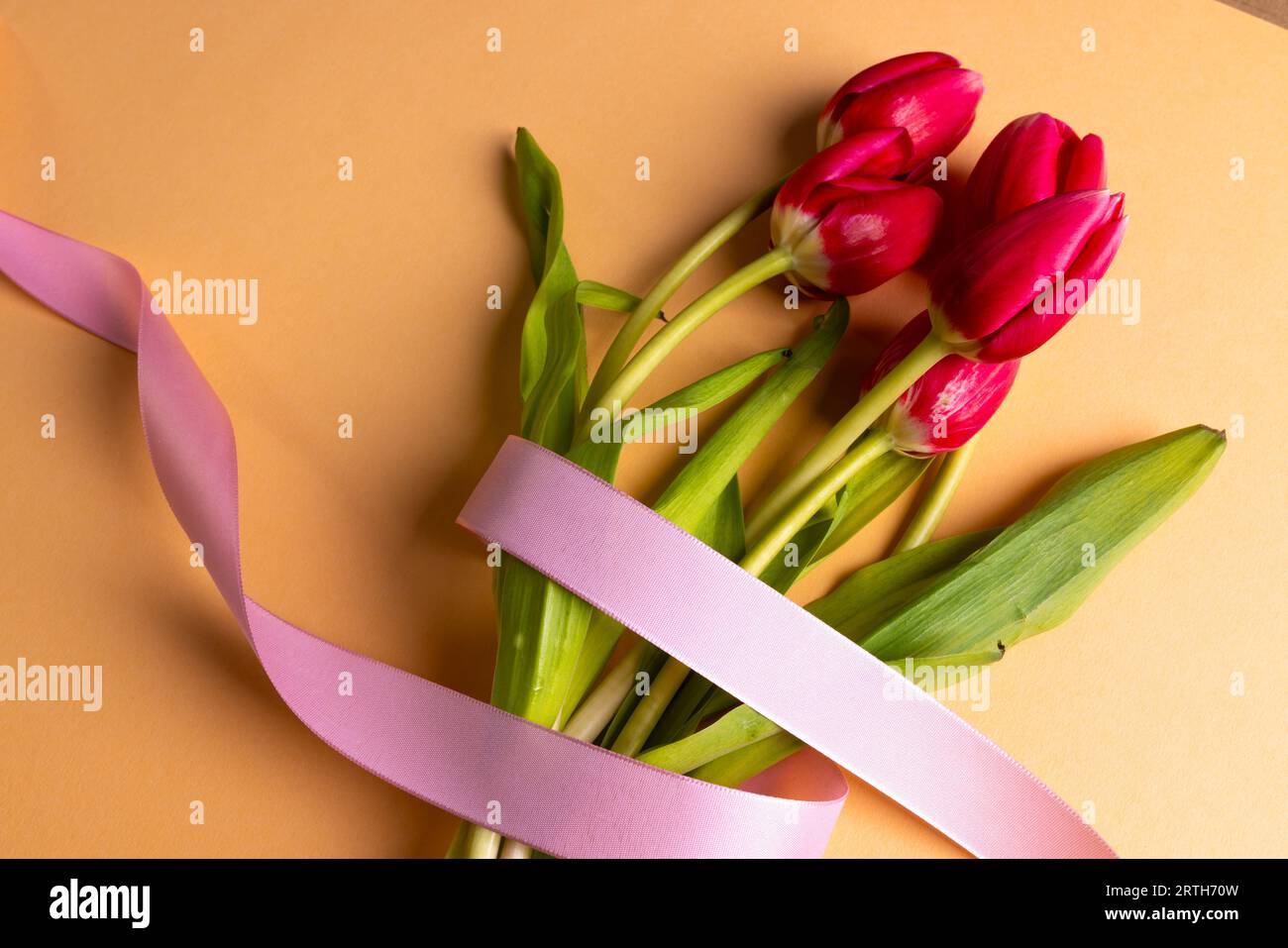 Bouquet de tulipes rouges avec ruban rose et espace de copie sur fond orange Banque D'Images