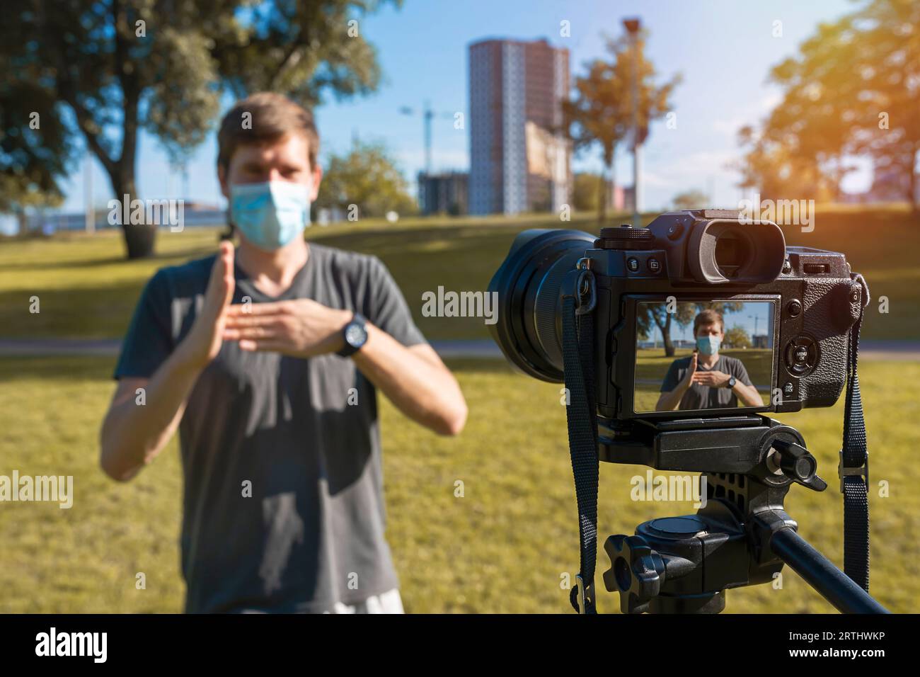 Un blogueur masculin portant un masque de protection tourne une vidéo avec un appareil photo numérique à l'extérieur par une journée ensoleillée Banque D'Images