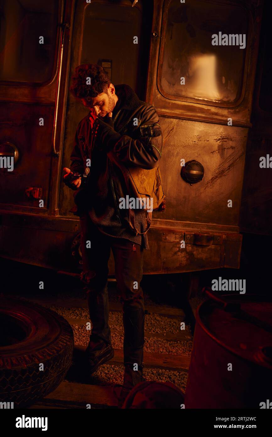 homme réfléchi regardant la pièce de rechange d'une voiture de métro rouillée dans un souterrain post-apocalyptique Banque D'Images