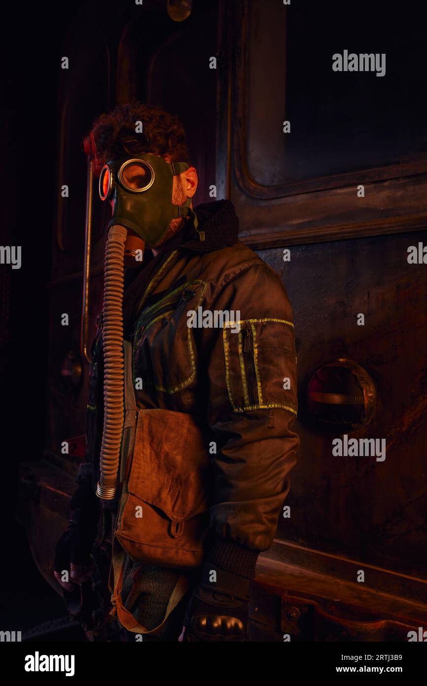 homme en veste sale et masque à gaz près d'un wagon rouillé de métro dans un tunnel souterrain abandonné Banque D'Images